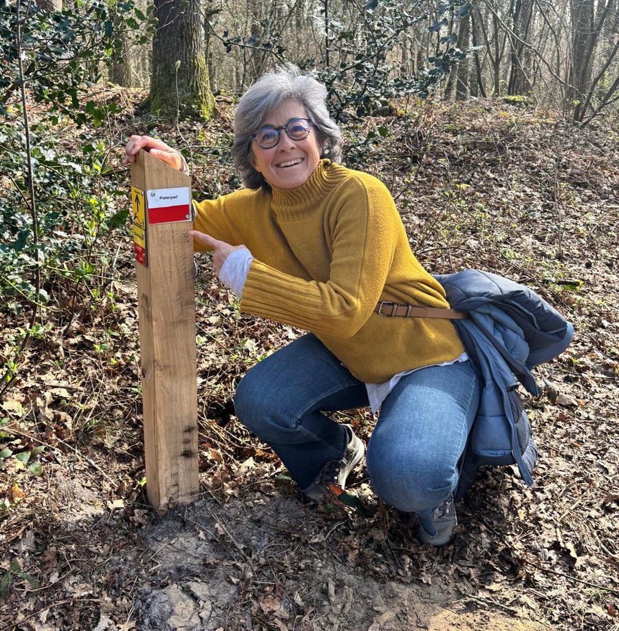 Mònica wijst naar een wegwijzerpaal op het Pieterpad in het bos